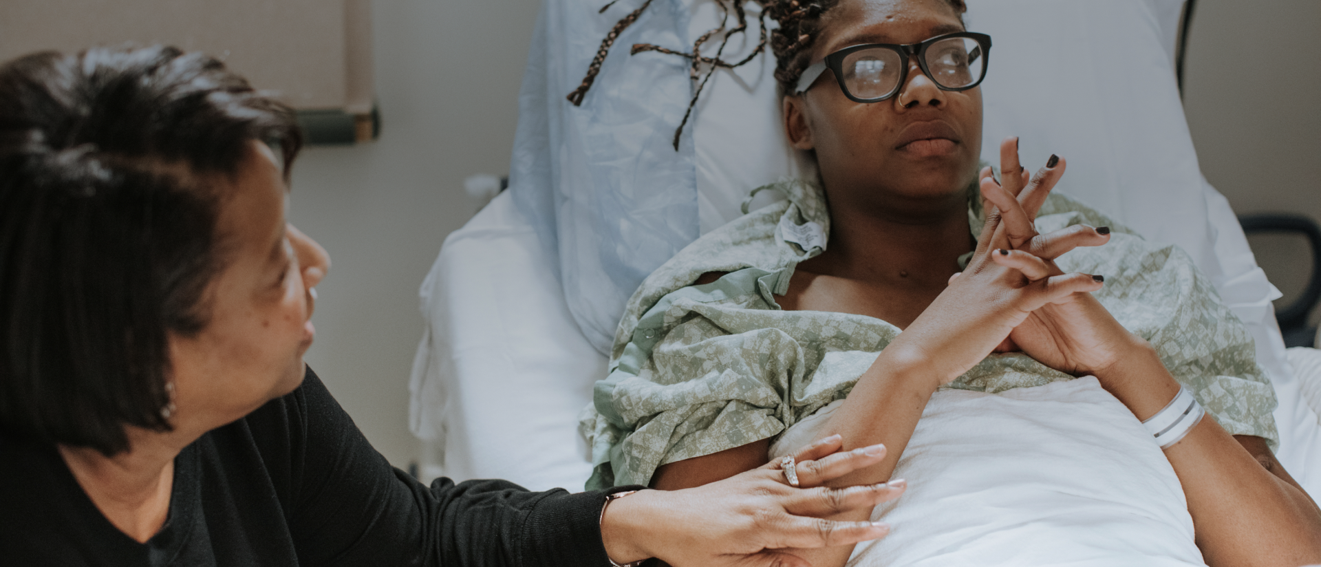 Eine im Bett liegende Patientin spricht mit einer Angehörigen 